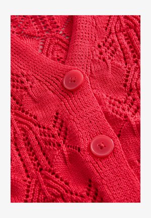 Rød strikket cardigan med blondermønster, V-udskæring og to skinnende røde knapper. Teksturen er detaljeret og indviklet med åbne masker.