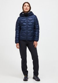 Tmavě modrá prošívaná péřová bunda s kapucí a předním zipem. Nositelná s černými kalhotami a robustními botami pro venkovní použití.