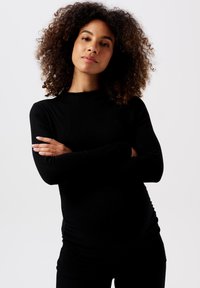 Sort langærmet top lavet af et glat materiale, med en rund halsudskæring og en let figursyet design, båret med sorte bukser.