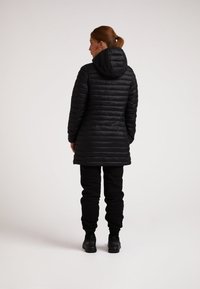 Cappotto nero imbottito con cappuccio, caratterizzato da un design trapuntato. Abbinato a pantaloni neri e stivali, mostrato di spalle.