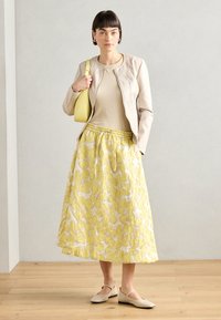 Veste en cuir beige, haut beige, jupe à motif floral jaune, et chaussures de couleur claire. Combinaison de textures et de couleurs dans un design superposé.