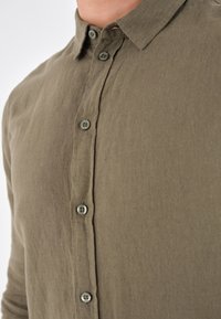 Camicia in lino verde oliva con design a bottoni, caratterizzata da cinque bottoni in contrasto e colletto. Tessuto testurizzato, vestibilità casual.