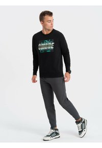 Sudadera de algodón negra con un estampado gráfico, combinada con pantalones grises de corte ajustado y zapatillas de caña alta en gris verdoso. Textura suave, diseño ajustado.