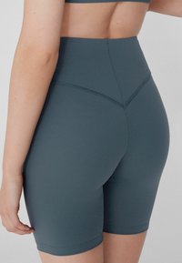 Shorts de vélo taille haute en vert foncé, fabriqués à partir d'un tissu extensible. Présentent des coutures sans coutures et un design lisse et ajusté.