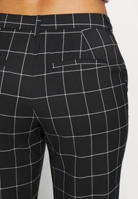 Black and white checkered trousers with a smooth texture, featuring back pockets and a fitted design. Tailored, structured shape.