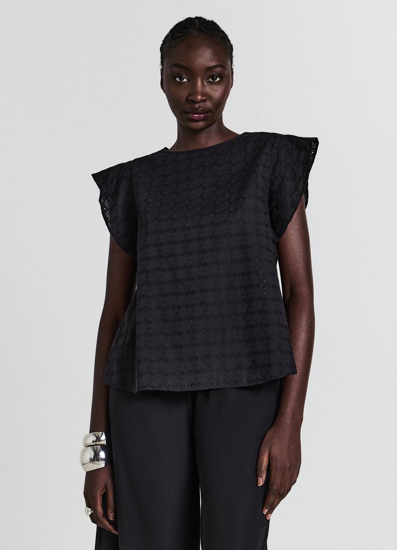 Haut noir texturé avec des manches courtes à volants et une coupe carrée, arborant un motif en losanges, porté avec un pantalon noir simple.