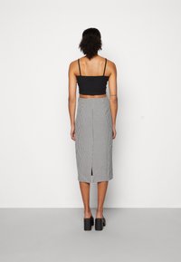 Svart kortärmad topp och knälång, rutad pennkjol med slit bak. Modellen bär kraftiga svarta klacksandaler.