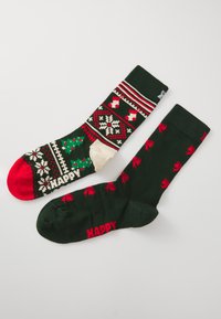 Chaussettes de Noël vertes et rouges en matière tricotée. Présentent des motifs saisonniers, avec le texte "Joyeux", et des designs variés sur chaque chaussette.