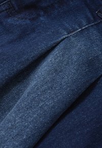Donkerblauwe denimstof met een gladde textuur en een lichte glans, met een gevouwen gedeelte en subtiele kleurvariaties door het geheel.