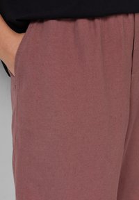 Helle rosa, weiche Stoffhosen mit einem elastischen Bund, ausgestattet mit Seitentaschen und glatter Textur. Nahaufnahme des Materials.