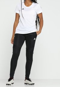 White short-sleeve athletic shirt with black logo; black fitted pants with striped accents; worn with black and white cleats on a neutral background.