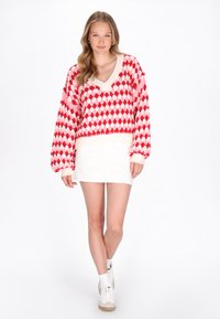 Rød og hvid mønstret oversized sweater med V-hals og ribbed ærmer, parret med en hvid mini nederdel og hvide høj-top sneakers.