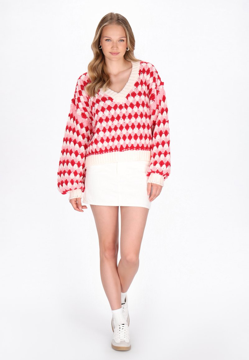 Rød og hvid mønstret oversized sweater med V-hals og ribbed ærmer, parret med en hvid mini nederdel og hvide høj-top sneakers.