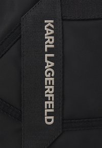 Czarna torba nylonowa o teksturowanej powierzchni. Posiada wyraźne srebrne logo "KARL LAGERFELD" oraz czysty, geometryczny wzór uchwytu.