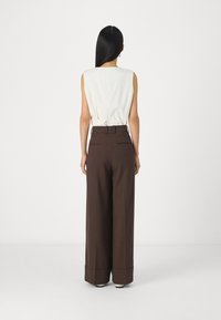 Haut sans manches blanc avec un dos cintré, associé à un pantalon à taille haute marron à jambes larges avec ourlet à revers et poches arrière.