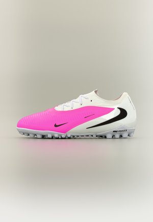 Chaussure de football Nike React blanche et rose avec logos Swoosh noirs et semelle texturée pour terrain synthétique, montrée en profil latéral sur fond neutre.