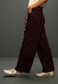 Široké nohavice z marhuľového kordurového látky s bočnými vreckami, doplnené striebornými športovými topánkami. Pás zdobí fialová šatka s bodkami.