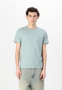 Ανοιχτό πράσινο βαμβακερό μπλουζάκι με κοντά μανίκια και στρογγυλή λαιμόκοψη, με μικρή λεπτομέρεια λογότυπου στο στήθος και άνετη εφαρμογή.