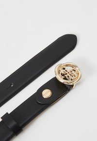 Ceinture en cuir noir avec une boucle ronde en ton or présentant un design complexe, et un clou de logo doré de la marque sur la sangle.