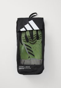 Sac en mesh noir contenant des gants de gardien de but verts et noirs. Le sac dispose d'une fermeture à rabat et d'un logo Adidas blanc sur le devant.