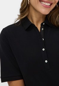 Sort polo shirt lavet af blødt stof, med krave, korte ærmer og en fire-knap lukning med kontrasterende hvide knapper.