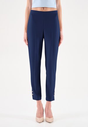 Pantalon sur mesure bleu marine avec une silhouette ajustée, doté d'accents en métal doré aux poignets et d'une texture lisse et élégante.