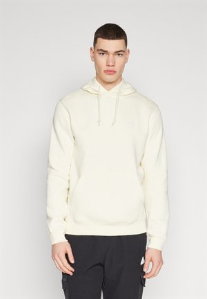 Hanorac off-white din material moale, având o carcasă frontală, glugă cu șnur și un mic logo pe piept. Asortat cu pantaloni închiși la culoare.