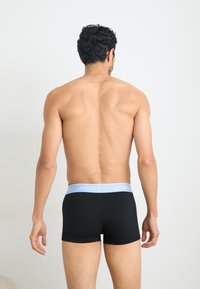Black boxer briefs with a light blue Lacoste logo waistband, displaying a smooth fabric and fitted design from a rear perspective.