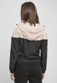 Svart og lys rosa hettejakke med kontrasterende design, elastiske mansjetter og hem, og en glatt, vannavstøtende tekstur.