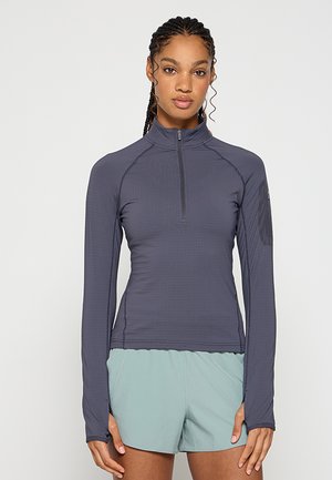 Koszulka z długim rękawem i zamkiem błyskawicznym w ciemnoszarym kolorze, wykonana z fakturowanej, elastycznej tkaniny. Posiada rękawy raglanowe oraz detal w postaci bocznych paneli.