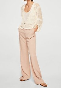 Lekki, przezroczysty kardigan w kremowym kolorze w poziome paski, sparowany z luźnymi, jasnoróżowymi spodniami i sandałami na paski.