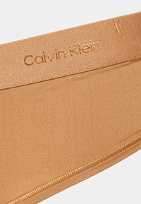Roupa interior Calvin Klein numa cor bege, apresentando uma textura suave e uma cintura em cetim com detalhes de logótipo bordado.