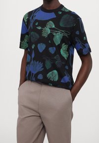 Czarny t-shirt z krótkim rękawem, ozdobiony żywym kwiatowym wzorem w odcieniach niebieskiego i zielonego. Miękka tkanina; luźny krój. Połączony z jasnoszarymi spodniami.