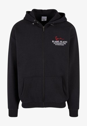 Čierna zipová mikina s kapucňou, ktorá má predné vrecko, rebrované manžety a lem, a vyšívané logo v bielej a červenej farbe. Mäkká, textúrovaná tkanina.