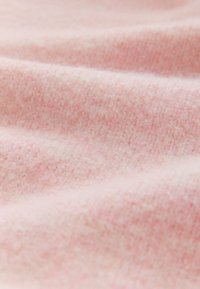 Tissu tricoté rose doux et duveteux avec une surface légèrement texturée et des plis doux créant des ombres subtiles.