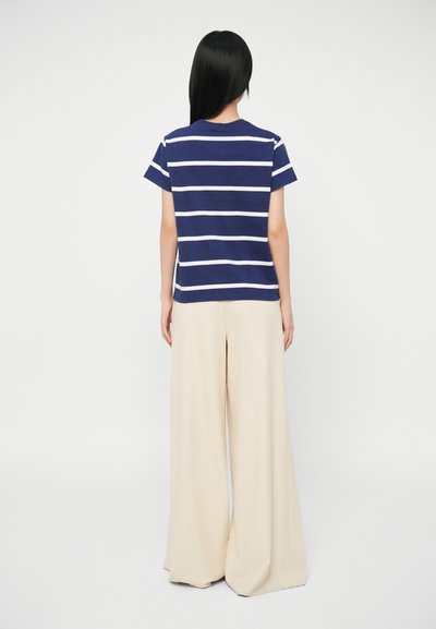 Ναυτικό και λευκό ριγέ μπλουζάκι με κοντά μανίκια, συνδυασμένο με μπεζ παντελόνι σε φαρδιά γραμμή. Υλικό βαμβάκι, άνετη εφαρμογή.