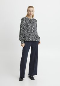 Sorte og hvide blomsterbluse med puffede ærmer, knaplukning foran, parret med mørkeblå vide bukser og sorte blokhæl ankle boots.