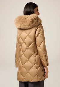 Tan puffervest med diamantquiltet mønster, med hætte foret med kunstpels. Glat, skinnende tekstur med lange ærmer og sideslids.