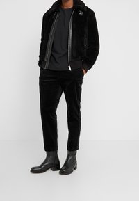 Schwarze Kunstfell-Bomberjacke mit einem Lederreißverschluss, kombiniert mit schwarzen Cordhosen und schwarzen Leder-Stiefeletten.