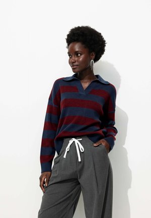 Pull en tricot rayé bleu marine et bordeaux avec un col en V et un col; associé à un pantalon large gris clair avec un cordon blanc.