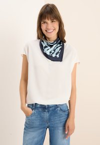 Foulard di seta blu navy con motivo astratto blu chiaro indossato attorno al collo, abbinato a una blusa bianca a maniche corte e pantaloni in denim blu.