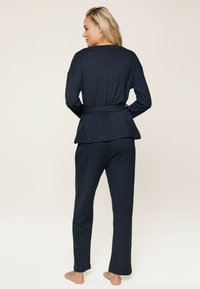 Completo da loungewear blu scuro composto da un top a maniche lunghe con cintura e silhouette a peplo, abbinato a pantaloni dritti in una texture morbida.