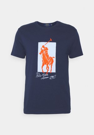 Marineblaues T-Shirt mit orangefarbener Polospieler-auf-Pferd-Grafik und dem Text "Polo Ralph Lauren 1967" in Weiß unterhalb der Illustration.