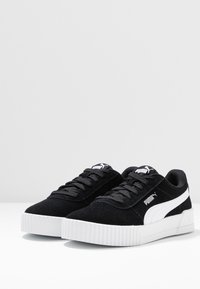 Černé semišové tenisky s bílou gumovou podrážkou a výrazným logem Puma. Mají černé tkaničky a texturovaný design svrchní části.