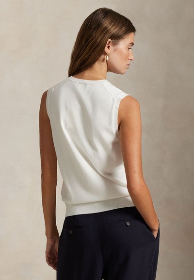 Top bianco senza maniche con finitura testurizzata, scollo rotondo e orlo a costine. La modella ha i capelli sciolti e indossa pantaloni scuri.