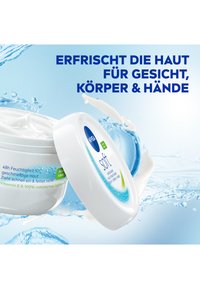 Moisturizing cream in a white container with blue accents; features text about hydration, contains Vitamin E and jojoba oil.