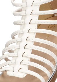 Sandal de tiras blanca con correas de cuero, diseño de punta abierta, forro interior beige y sutiles acentos metálicos en la suela.