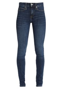 Jeans ajustados de denim azul oscuro, con costuras en contraste, un diseño clásico de cinco bolsillos y una cremallera con cierre de botón.