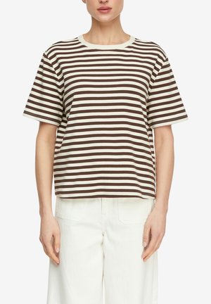 Kobieta ubrana w brązowo-biały poziomo w paski krótki rękaw koszuli i białe spodnie, stojąca na jednolitym białym tle.