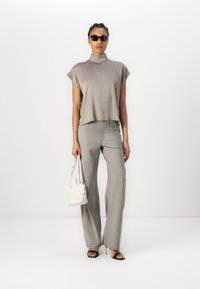 Top grigio a maniche corte e colletto alto abbinato a pantaloni larghi grigi chiari. Occhiali da sole neri e una piccola borsa bianca completano il look.